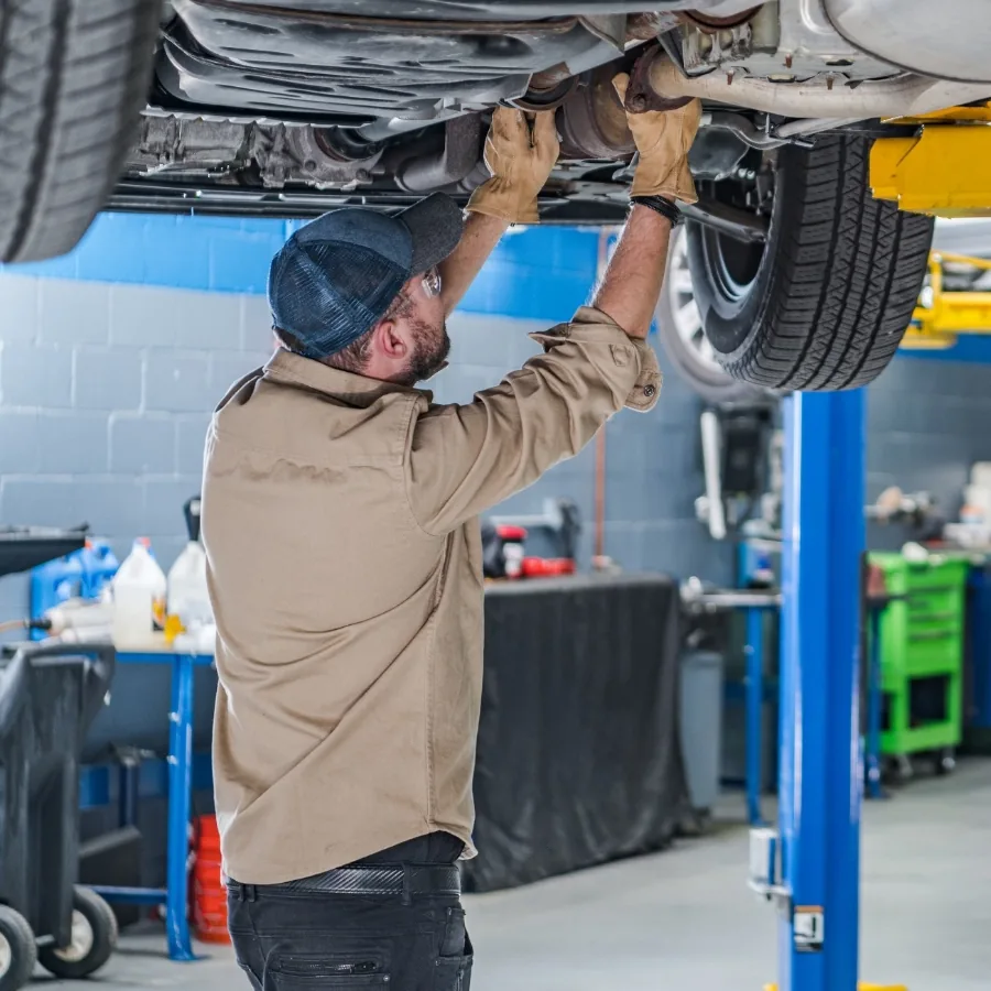 An auto technician servicing the undercarriage of a car raised on a lift in a professional service garage