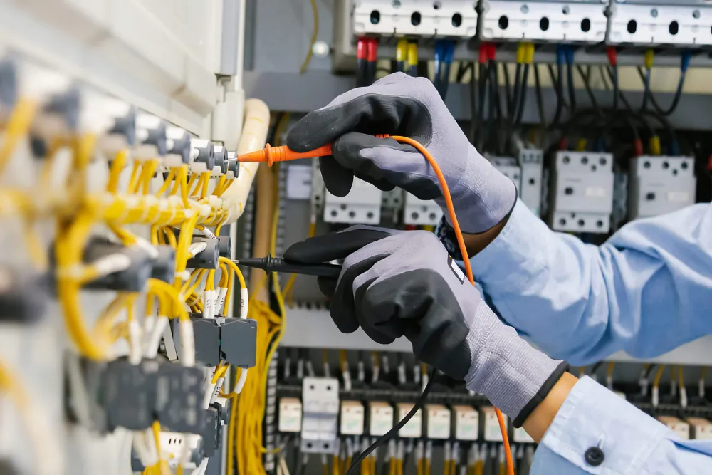 Close-up of an electrician's gloved hands wiring an industrial electrical control panel