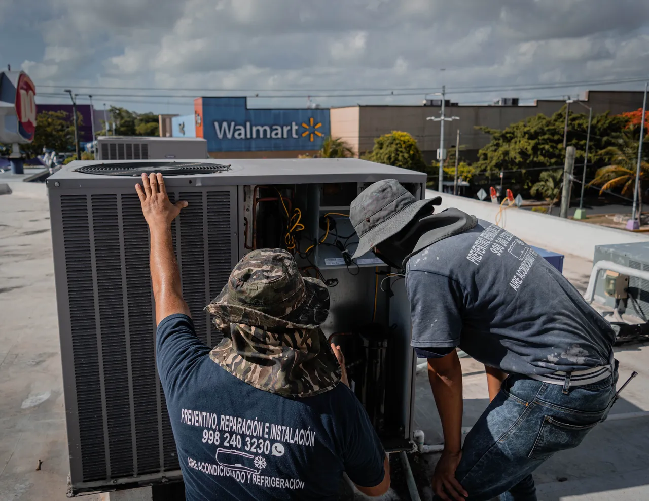 Two HVAC technicians servicing a rooftop air conditioning unit on a sunny day