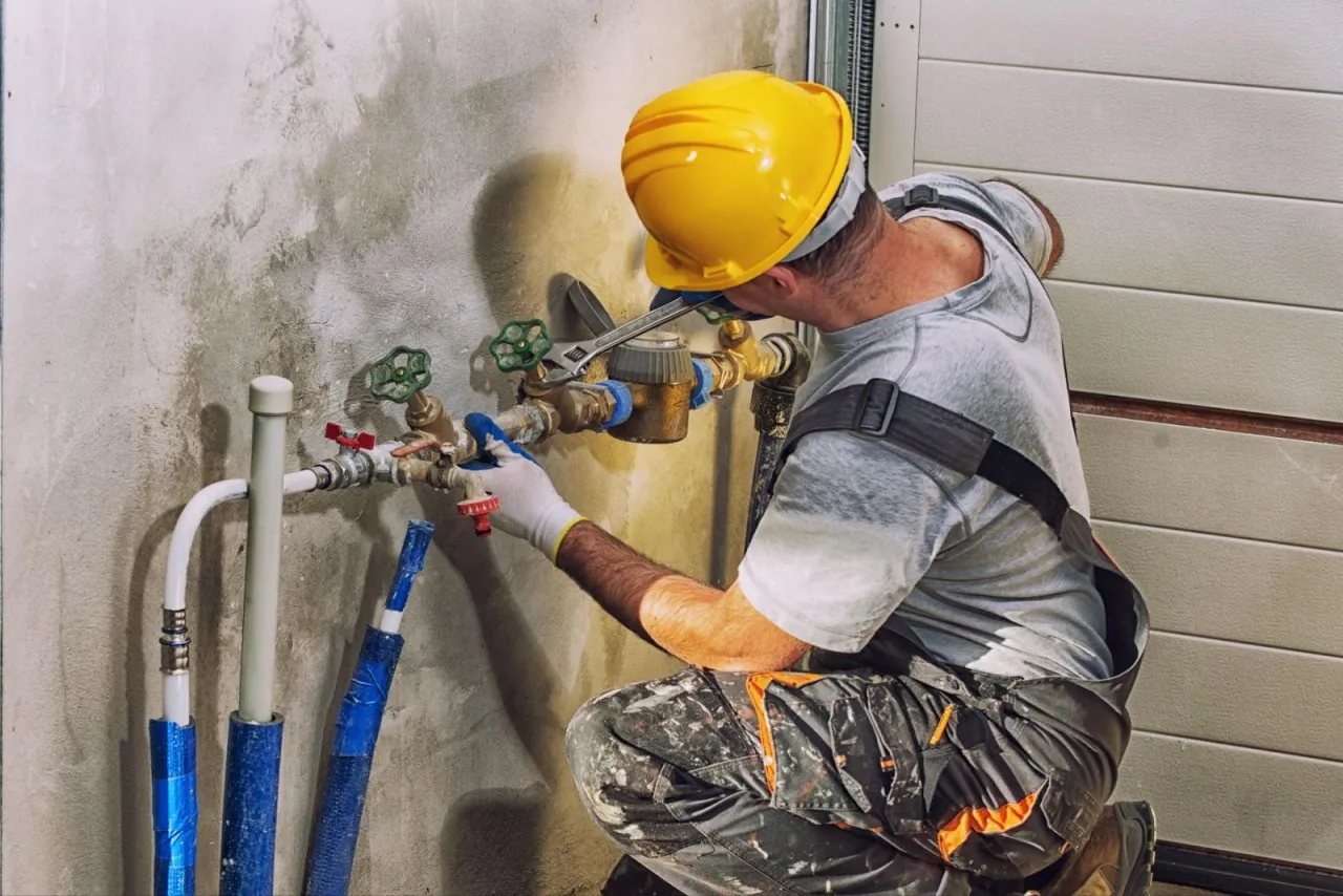 A plumber in a hard hat using a wrench on copper shutoff valves and supply lines mounted to a wall