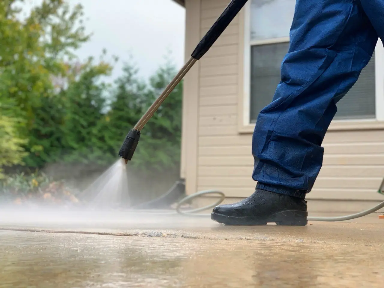 A pressure washing technician cleaning a concrete patio in front of a residential home
