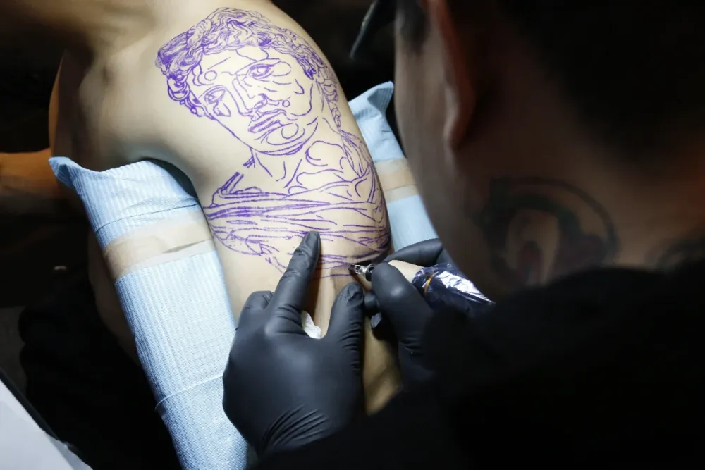 A tattoo artist outlining a detailed stencil on a client's shoulder during a tattoo session